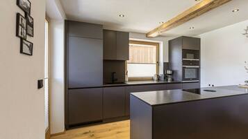 A modern kitchen with dark cabinetry, a central island, and built-in appliances.
