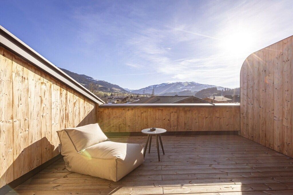 En træterrasse med en sofa og et lille bord, med udsigt over et bjergrigt landskab.