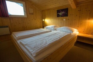 A wooden cabin room with a bed, a window, and a wall-mounted picture.