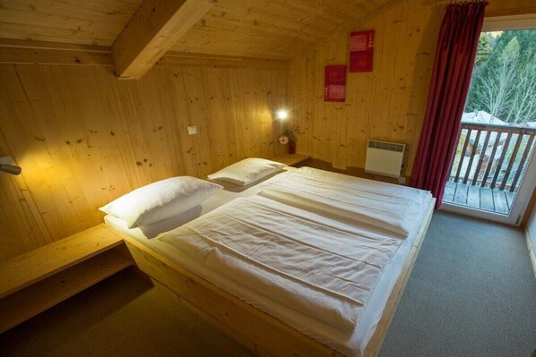 A wooden cabin room with a bed, a nightstand, and a window with a view of trees.