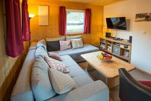 A cozy living room with a sofa, a television, and a coffee table with fruit.