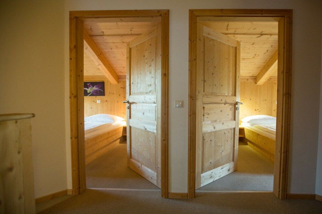 Ein Zimmer mit zwei Holztüren, die zu einem Schlafzimmer mit einem Bett und einem an der Wand befestigten Fernseher führen.
