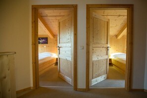 A room with two wooden doors leading to a bedroom with a bed and a wall-mounted television.
