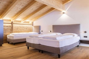 Quarto com duas camas, vigas de madeira no teto e luminária na parede.