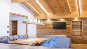 Ein modernes Interieur mit Holzbalkendecke, einem Wand-Fernseher, einer hölzernen Bank und einem Sofa mit gemustertem Kissen.