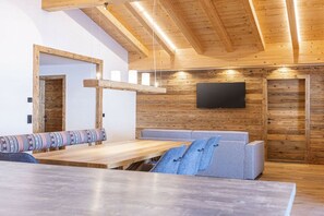 Interior moderno com teto de madeira, TV de tela plana na parede, um banco de madeira e um sofá com almofada estampada.