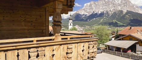 Un balcón de madera con vistas a la montaña, una iglesia con un campanario y un pueblo abajo.