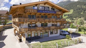 Ein mehrstöckiges Holzgebäude mit Balkonen, beschriftet mit 'ALPS RESORTS', inmitten einer gebirgigen Landschaft.