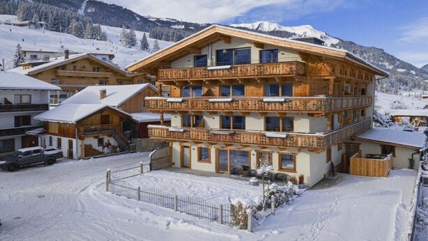Ein mehrstöckiges Holzchalet mit Balkonen, umgeben von schneebedeckten Bergen.