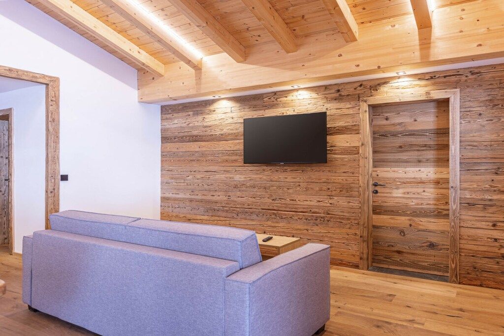 A modern interior with a wooden wall, a flat-screen TV, and a grey sofa.