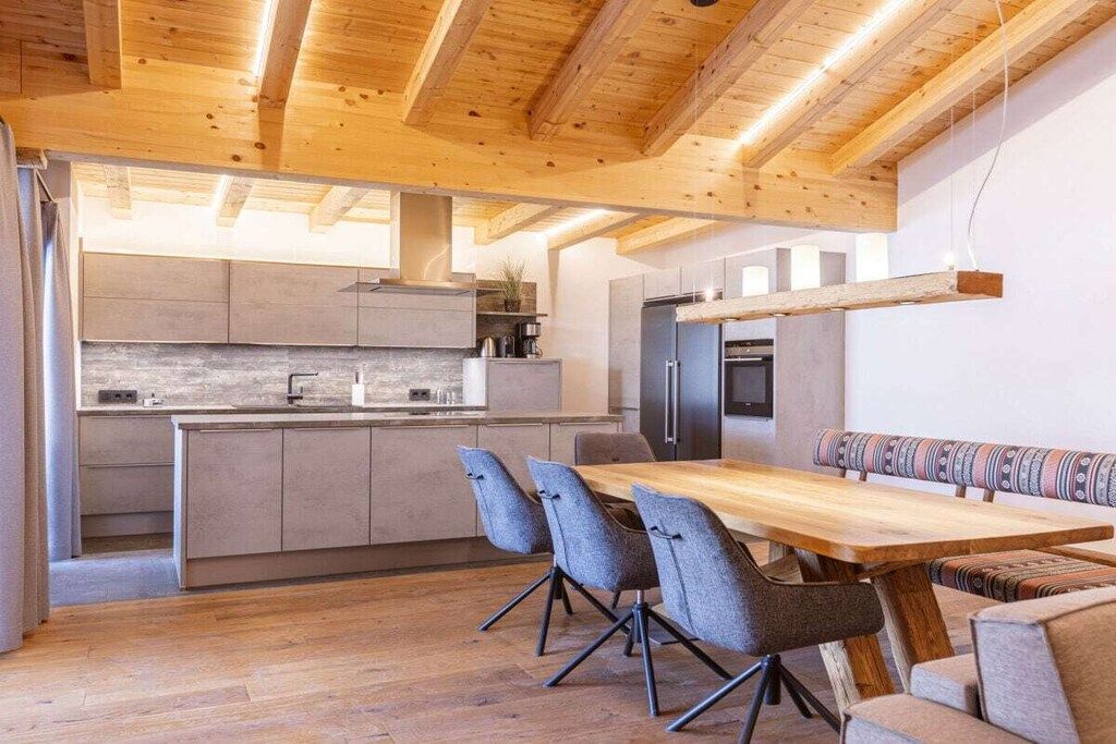 A modern kitchen with wooden beams, a dining area with a wooden table and chairs, and a built-in bench.