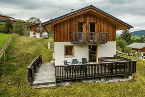 Een houten chalet met twee verdiepingen, een balkon, een terras en uitzicht op het omliggende landschap.