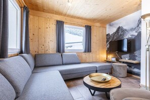 Een moderne woonkamer met een hoekbank, een ronde salontafel en een grote tv aan de muur.