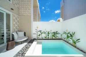 A modern outdoor pool area with a white infinity pool, a seating area with a white sofa and cushions, and a row of tall plants against a white wall. - Surya TN Villa by Betterplace (Pecatu)