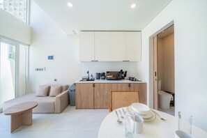 A modern kitchen with white cabinets, a dining area with a round table, and a sofa. - Surya TN Villa by Betterplace (Pecatu)