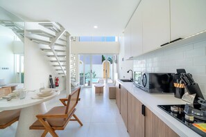 Eine moderne Küche mit einer zentralen Kochinsel, einem Essbereich mit einem Stuhl und einer Treppe, die zu einem Außenbereich führt.