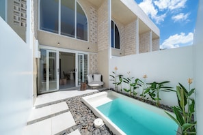A modern outdoor pool area with a clear blue pool, surrounded by a pebble border, and a seating area with a sofa and table. - Surya TN Villa by Betterplace (Pecatu)