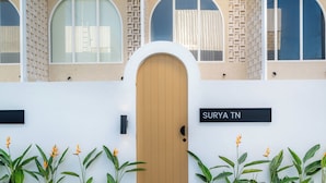 Un edificio con una puerta de madera, un letrero que dice 'SURYA TN' y una fila de plantas al frente.