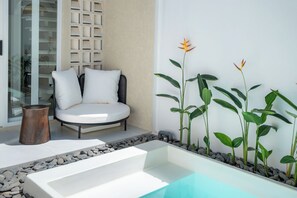 A modern outdoor seating area with a white sofa and cushions, a small wooden table, and a rectangular planter with green plants and a single flower. - Surya TN Villa by Betterplace (Pecatu)