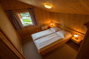 A wooden cabin room with a bed, two bedside lamps, a window with curtains, and a ceiling light. - Cabin in Annaberg with swimming pool (Annaberg)
