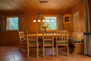 A wooden interior with a dining table, chairs, a bench, and a window with curtains. - Cabin in Annaberg with swimming pool (Annaberg)