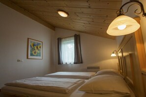 Een kamer met twee bedden, een raam met gordijnen, een schilderij aan de muur en een plafondlamp.