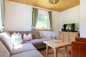 Ein Wohnzimmer mit einer Couch, einem Holztisch, einem Fernseher und einem Fenster mit Vorhängen.