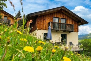 Eine Holzhütte mit einem Balkon, umgeben von viel Grün und Blumen.