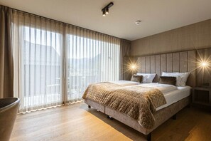 Een moderne slaapkamer met een groot bed, een nachtkastje en uitzicht door dunne gordijnen.