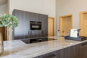 Eine moderne Küche mit dunklen Schränken, einem eingebauten Backofen und einer Arbeitsplatte mit einer Kaffeemaschine.