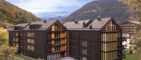 A multi-story building with balconies, a swimming pool, and a mountainous backdrop.