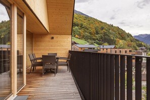 A wooden deck with a table and chairs, overlooking a hillside with houses. - Apartment in Schruns with swimming pool (Schruns)