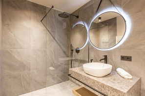 Une salle de bain moderne avec un grand miroir, un lavabo rond et une douche à parois de verre.
