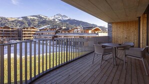 Eine Holzterrasse mit Sitzgelegenheiten im Freien, mit Blick auf eine gebirgige Landschaft mit schneebedeckten Gipfeln.