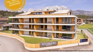 Ein modernes Hotel mit zweigeschossiger Bauweise, Balkonen und einem Bergpanorama im Hintergrund.