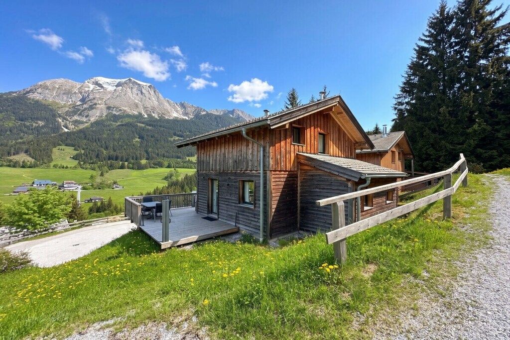 Een houten chalet met een terras, omringd door een bos en bergen.