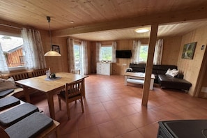 Ein Holzinnenraum mit einem Esstisch, Bänken, einer Couch und einem an der Wand befestigten Fernseher.