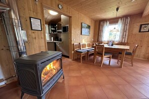 Ein Holzinnenraum mit Holzofen, Esstisch, Stühlen und einer Küchenzeile.