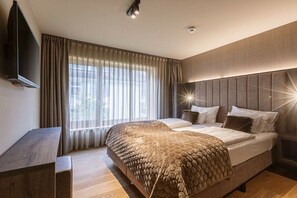 A modern hotel room with a large bed, a flat-screen TV, and a large window with curtains. - Apartment in Schruns with swimming pool (Schruns)