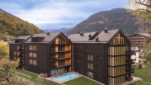 Un immeuble à plusieurs étages doté de balcons, d’une piscine et surplombant un paysage montagneux.