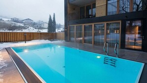 Une piscine avec une terrasse en bois et une vue sur un immeuble doté de grandes fenêtres et de balcons.