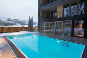 A swimming pool with a wooden deck and a view of a building with large windows and balconies. - Apartment in Schruns with swimming pool (Schruns)