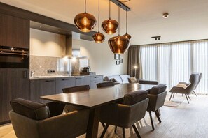 A modern kitchen with a dining area, featuring a large table and chairs, pendant lighting, and a view of the outdoors through large windows. - Apartment in Schruns with swimming pool (Schruns)