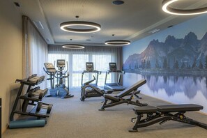 Ett gym med konditionsmaskiner, styrketräningsmaskiner och en väggmålning som föreställer ett berglandskap.
