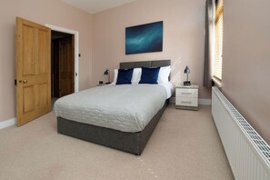 Un dormitorio con una cama, mesitas de noche, un radiador y una puerta.