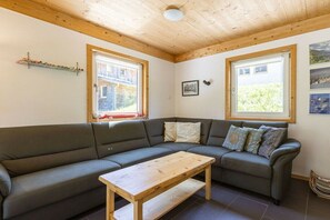 A room with a dark green sofa, a wooden coffee table, and two windows with wooden frames. - Cabin in Annaberg with swimming pool (Annaberg)