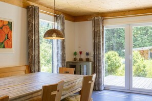 A dining area with a table, chairs, a hanging light fixture, and a view through a glass door to an outdoor deck. - Cabin in Annaberg with swimming pool (Annaberg)