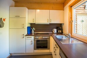Une cuisine de taille réduite avec des meubles blancs, un four en acier inoxydable, un évier et une fenêtre dotée d’un cadre en bois.