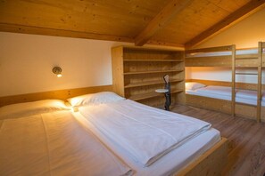 Quarto de cabana de madeira com beliches, uma mesa pequena e um armário com prateleiras.