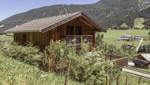 Una cabaña de madera con balcón, rodeada de vegetación y montañas.
